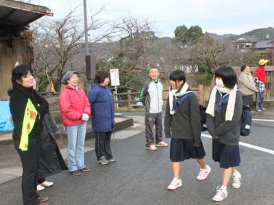 挨拶運動のため並んで立っている地域の方々と登校中の中学生2人の写真