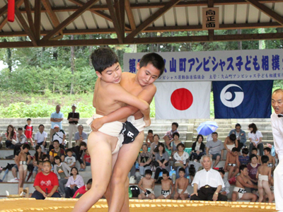 子供たちがお互いのまわしをつかみ、倒そうと力を込めている様子の写真