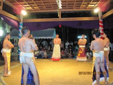 化粧まわしを付けた男性達が土俵に添って円になり腕を組んで見合っている写真