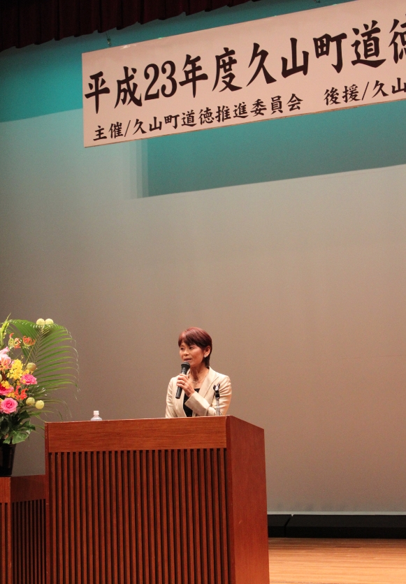 女性の講師が壇上で講演を行っている様子の写真