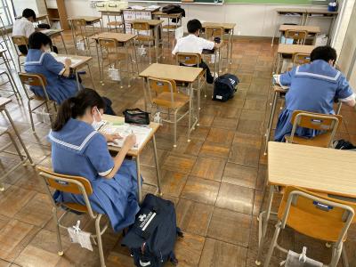 間隔をあけて席に座り学習している中学生たちの後ろ姿の写真