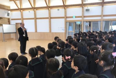 始業式でマイクを持って話をしている園長先生を見ている園児たちの写真