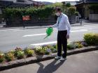 道路際の花壇にじょうろで水を上げるスーツ姿の男性の写真