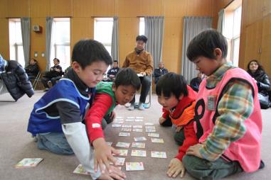 ゼッケンをつけた4名の子どもたちがかるた大会を行っている様子の写真