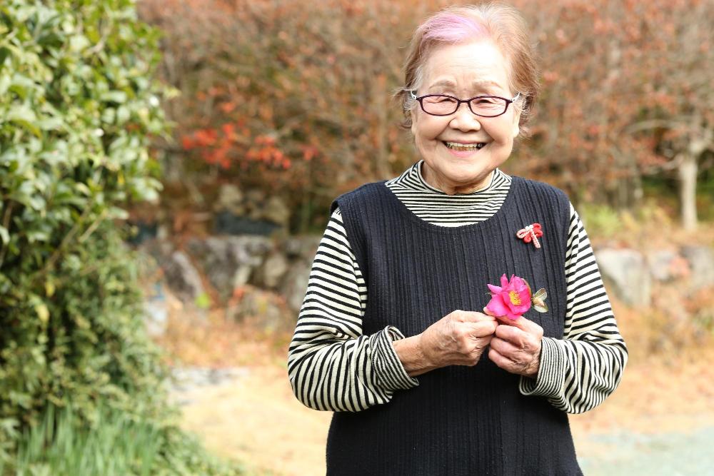 椿の花を持ち笑う敬子さん