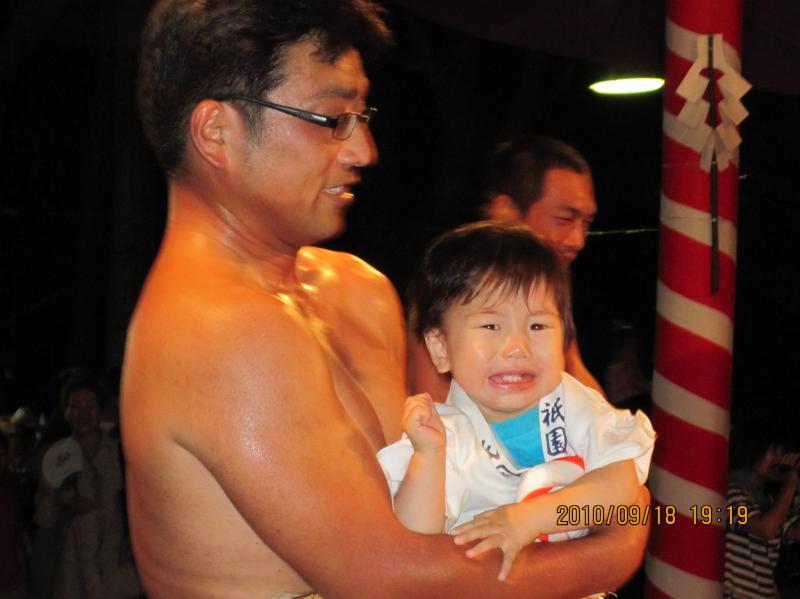 めがねをかけた上半身裸の男性が泣きそうな顔の子供を抱っこしている写真
