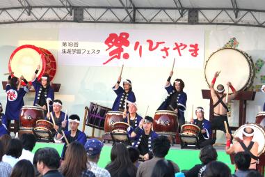 祭りひさやまのステージ上で法被姿で太鼓を披露する人たちと観客の写真