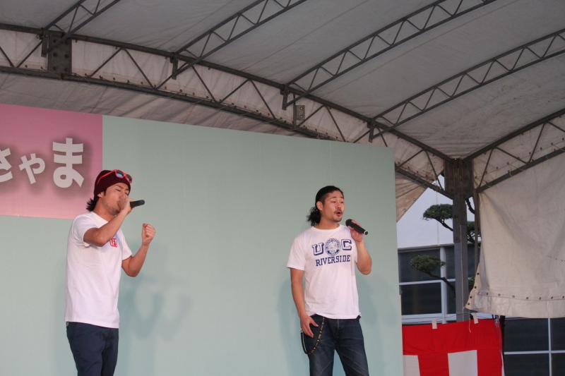 ステージ上で男性二人がマイクを持って歌っている写真