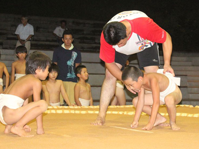 廻しをつけ土俵に上がった子供が、立ち合いの前の姿勢の指導を受けている様子の写真