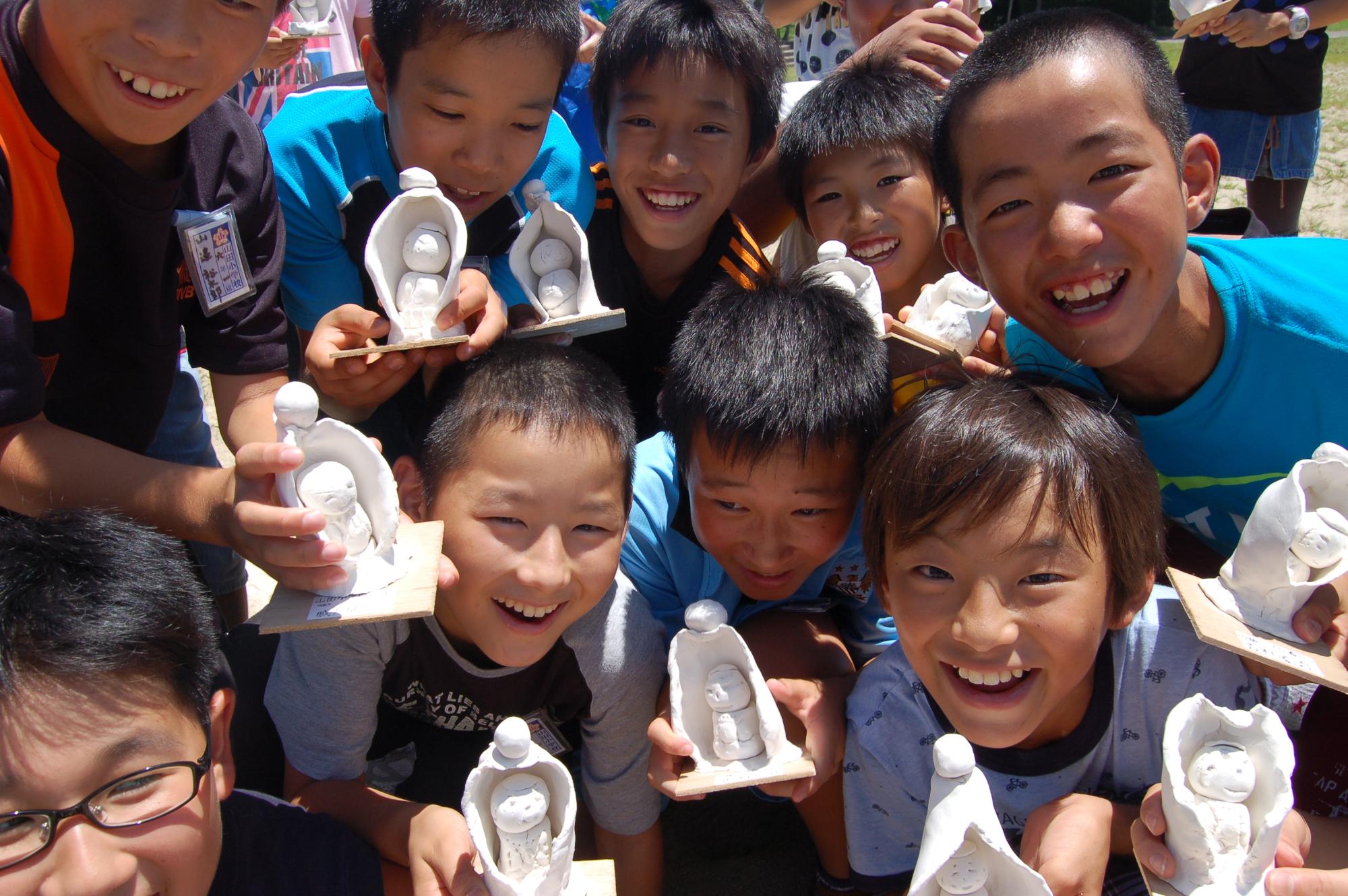 粘土で作ったお地蔵さんのようなものを持った子供たちが集まって笑顔で写っている写真