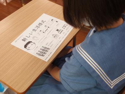 机の上に置かれた「新しい生活様式」のプリントを見ている生徒の写真