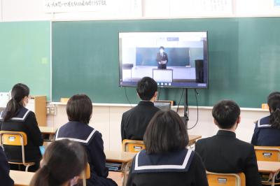 黒板の前のモニターに映し出された映像を着席して見ている生徒たちの写真
