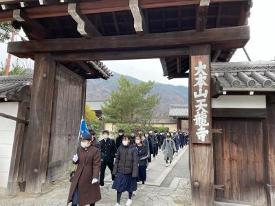 2列に並んだ中学生たちが旗を持った添乗員の後ろをついて歩き、大本山天龍寺の門を出ようとしている写真