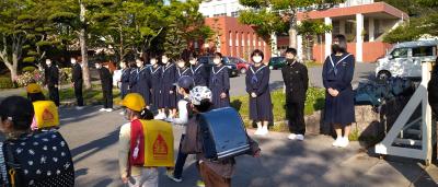 制服を着た中学生たちが横一列に並び、登校してくる小学生達に挨拶をしている様子の写真