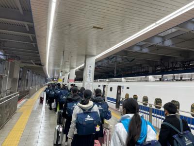 新幹線が停車している駅のホームを列をなして歩いている生徒たちの写真