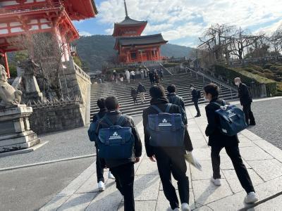 制服を着た男子学生たちが前方の階段の奥に見える赤い建物の方に向かって歩いている後ろ姿の写真