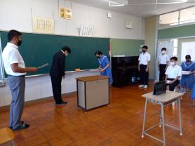 教室の黒板前で左側のスーツを着た男性と右側のセーラー服を着た女子学生が向かい合って礼をしている写真