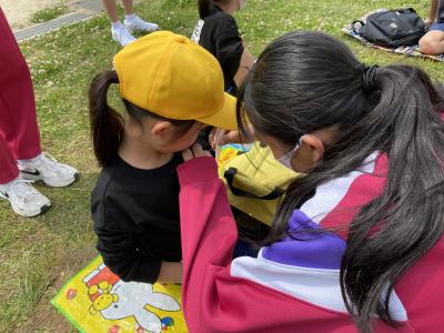 ピンク色のジャージを着た女子中学生が黄色い帽子を被った女の子の服に手をあてて、何か手伝っている様子の写真