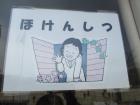 ほけんしつと書かれた文字の下に窓から手を振る女の子のイラストが描かれている写真