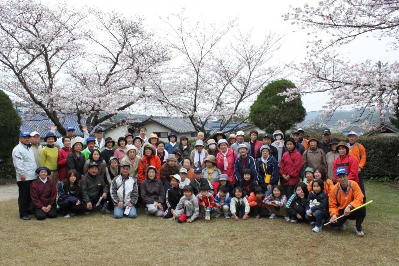 満開の桜の木の前で、桜ウォーキングに参加した参加者たちが並んでいる集合写真