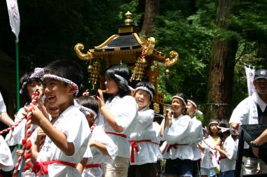 白色の法被を着て頭に鉢巻を巻いた子ども達が、神輿を担いで練り歩いている写真