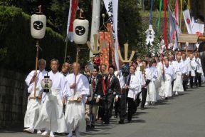 白色の法被や着物に袴を着た男性たちが列をなして練り歩いている催事の様子の写真