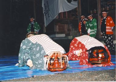 法被を着た5名の男性が立っている前に敷いたブルーシートの上に、2体の獅子舞が置いてある写真