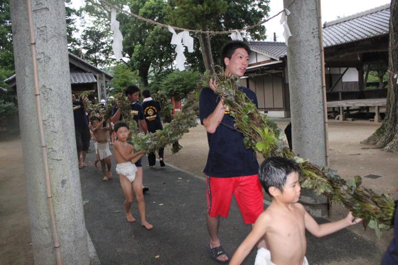 ふんどし姿の男の子たちと男性たちが綱を担いで、神社の鳥居の下をくぐって歩いている写真