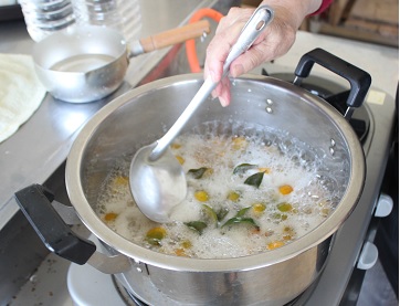 ぐつぐつ煮立っている金柑の鍋からお玉で灰汁を取っている写真